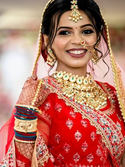 The perfect smile of a happy bride. She is wearing a classic Kundan choker set with a matching maang tikka and nath, creating a timeless and elegant bridal look.