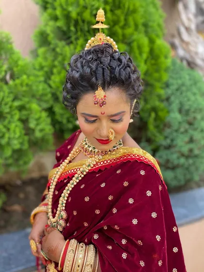 A traditional Maharashtrian bridal look. The hairstyle features tight curls forming a classic bun, adorned with traditional gold jewelry and a bindi for an authentic and elegant appearance.