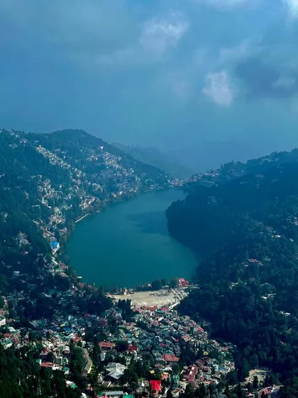 An aerial view of the stunning Naini Lake, surrounded by the bustling town of Nainital. Our lodge in nearby Pangot offers a peaceful retreat with easy access to this beautiful region.