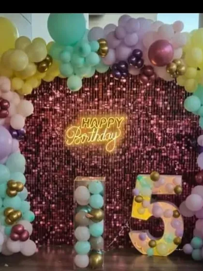 A pastel balloon arch against a pink sequin wall, featuring a light-up number '5'. This setup is perfect for adding sparkle to any venue.
