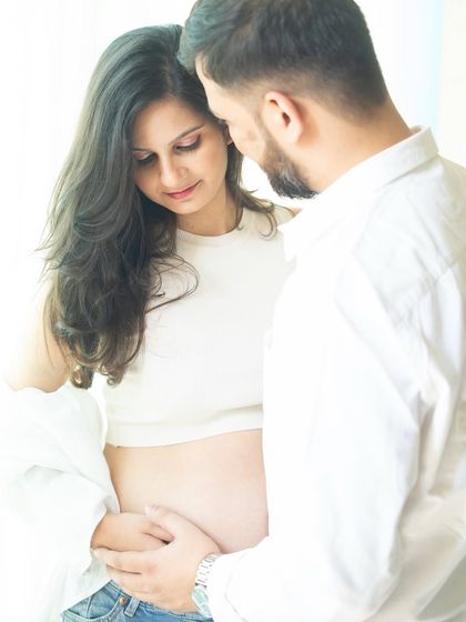 A close-up shot focusing on the couple's interaction and their hands gently holding the bump. The soft, natural light creates an intimate and warm atmosphere.