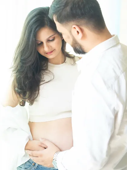 A close-up shot focusing on the couple's interaction and their hands gently holding the bump. The soft, natural light creates an intimate and warm atmosphere.