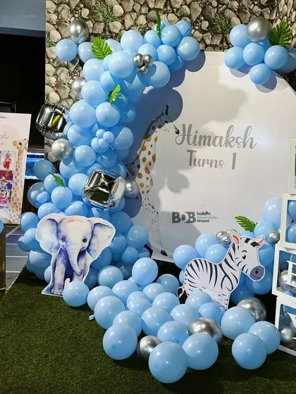 A gentle blue jungle theme for a first birthday. This setup includes elephant and zebra cutouts, 'BABY' blocks, and a balloon arch in shades of blue and silver.