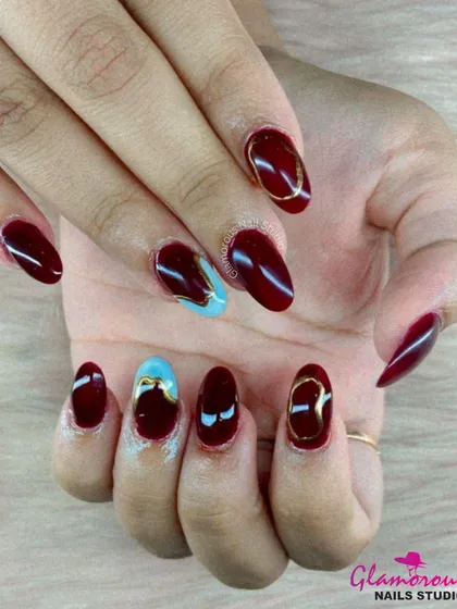 A rich and luxurious color combination. This set features deep, glossy maroon nails, with accent nails showcasing an abstract mix of light blue and gold for a truly artistic and high-fashion look.
