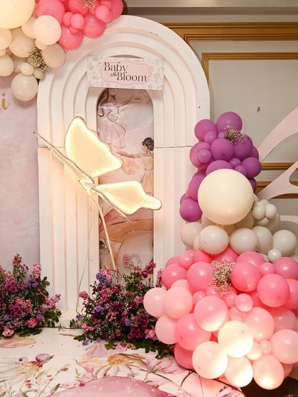 A detail shot of the butterfly-themed stage, focusing on the illuminated butterfly prop and the beautiful balloon clusters in shades of pink, purple, and white.
