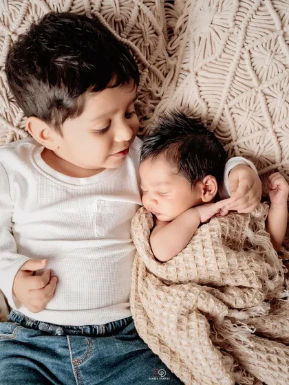 A tender moment between two brothers. The older brother lies down and gently holds his newborn baby brother, showcasing the beginning of a lifelong bond.