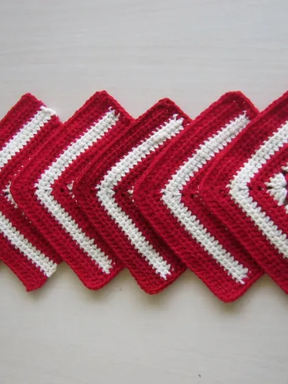 A set of red and white granny square coasters lined up in a row.