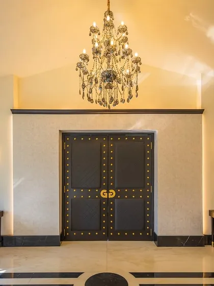The grand entrance doors of the Gallops banquet hall, seen from the inside. The space is flanked by elegant console tables and modern gold art pieces, with a magnificent chandelier overhead, creating a powerful and luxurious first impression.