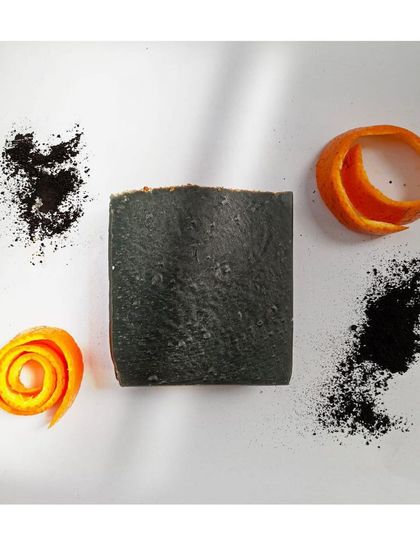 A flat-lay of the Charcoal Orange soap, showing its key ingredients: activated charcoal for detoxification and orange rind for a citrusy scent and gentle exfoliation.