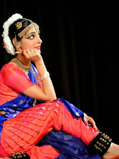 A seated pose from a Bharatanatyam performance, portraying a character in a moment of contemplation. The rich colors of the costume and traditional jewelry are integral to the visual storytelling.
