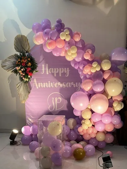 Another view of the purple-themed anniversary decor. The arrangement includes a clear plinth filled with balloons and a floral accent, adding layers of detail to the design.