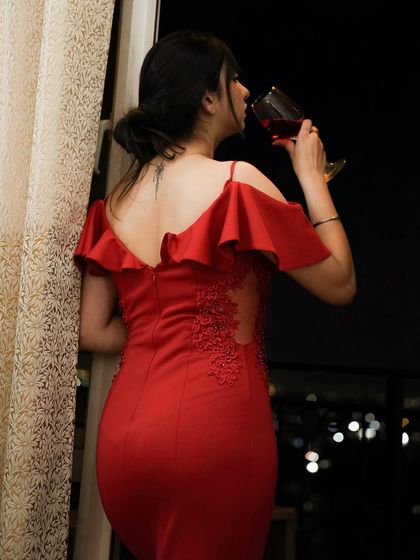 A beautiful shot from the back in a stunning red gown, looking out from a balcony at night.