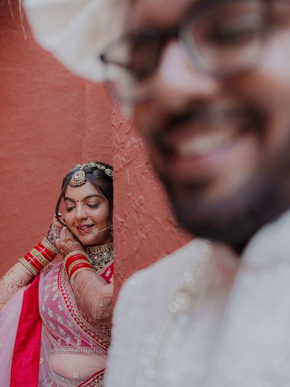 A creative shot with the groom's smiling face in the foreground, out of focus, and the bride beautifully framed behind him.