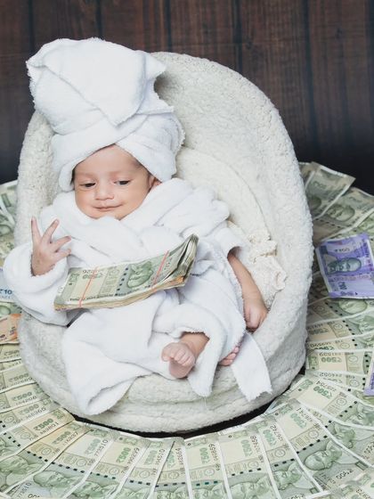 This little one is literally swimming in money. Dressed in a bathrobe with a towel on his head, he's the picture of a tiny tycoon.