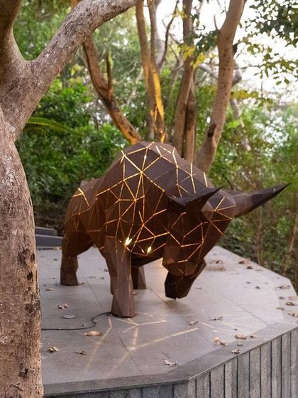 A large, origami-style bull sculpture with embedded lighting stands as a centerpiece in a garden. This fusion of traditional art form and modern craftsmanship creates a captivating and powerful landscape feature.