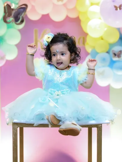 An adorable portrait of a one-year-old girl in a beautiful blue party dress, posing playfully for the camera. Our goal is to capture the sweet and fun side of your child's personality during their birthday photoshoot.