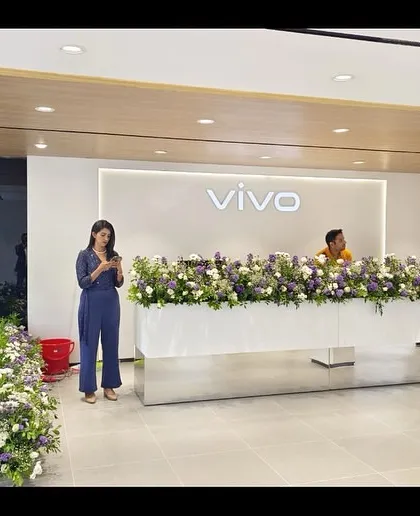 The main reception desk at a VIVO store, adorned with flowers for the opening. The minimalist design with backlighting and clean lines creates a strong brand statement right at the entrance.