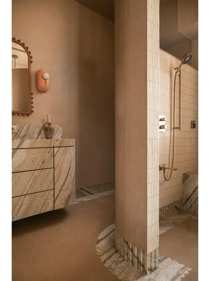 We call this bathroom a 'chic desert dream'. It features blush-toned micro-concrete walls and a monolithic vanity carved from veined Corteccia marble. The stone appears to trickle down onto the floor, creating a fluted skirting detail that is both organic and luxurious.
