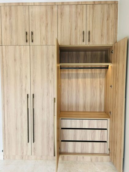 The interior of our laminate wardrobe reveals smart storage solutions, including drawers and a hanging rod with integrated lighting, all in a matching wood-grain finish.