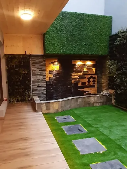 A backyard transformed with a backlit stone pathway, artificial grass, a vertical garden, and a stunning water feature.