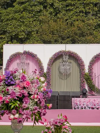The stage for the garden wedding, featuring three arches adorned with pink and purple flowers and crystal chandeliers.