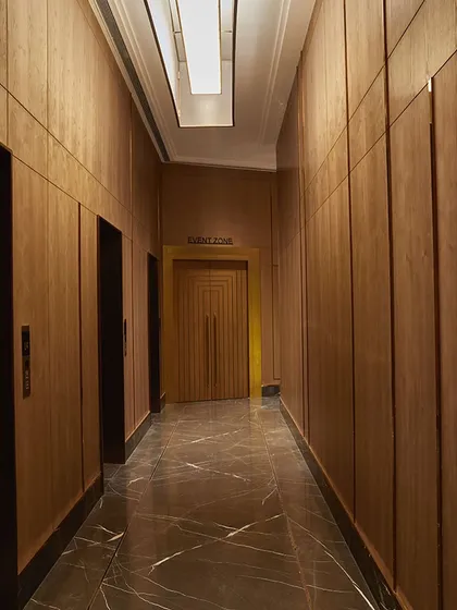 The interior corridor leading to the banquet hall features veneer-paneled walls and grand entrance doors, creating a sense of anticipation and grandeur.