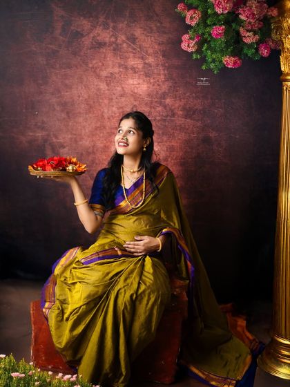 A moment of hopeful anticipation. The mother-to-be, dressed in a traditional saree, looks up as if dreaming of the future, holding a plate of offerings.