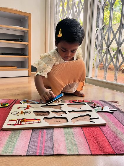 A young girl carefully places a puzzle piece into a transportation-themed board. The puzzle itself is a tool for order, as each piece has only one correct place, teaching logic and spatial awareness.