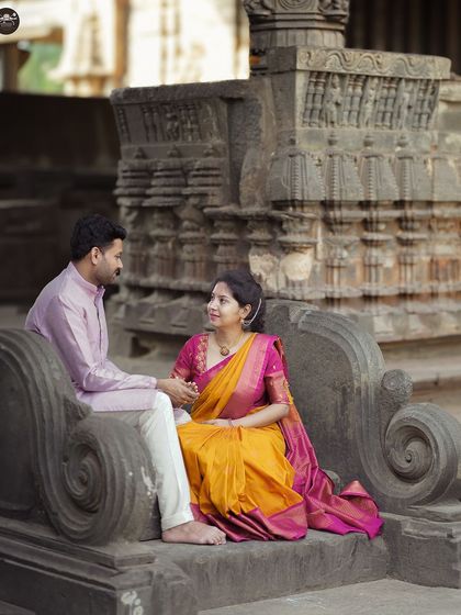 A beautifully composed shot of a couple in vibrant traditional attire, seated on an ornate stone bench at a temple. The colors and architecture create a rich, cultural feel.