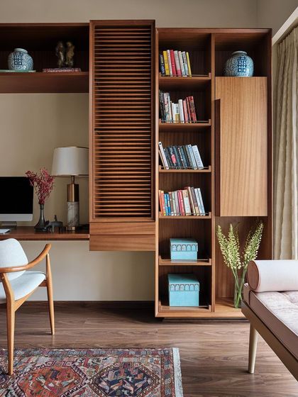 This study in the Peninsula Residence features custom-built wooden cabinetry with louvered details. The design provides a mix of open and closed storage, allowing for the display of books and decorative objects while keeping clutter hidden.