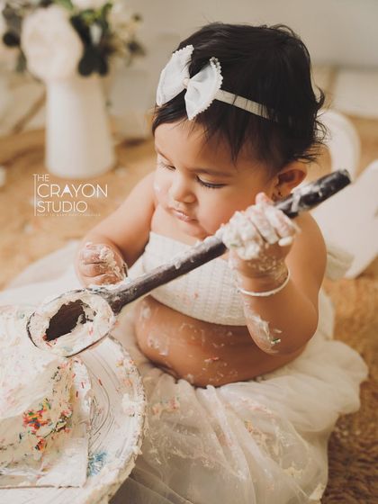A close-up of the cake smash fun. This little one is fascinated by the giant spoon and the messy cake.