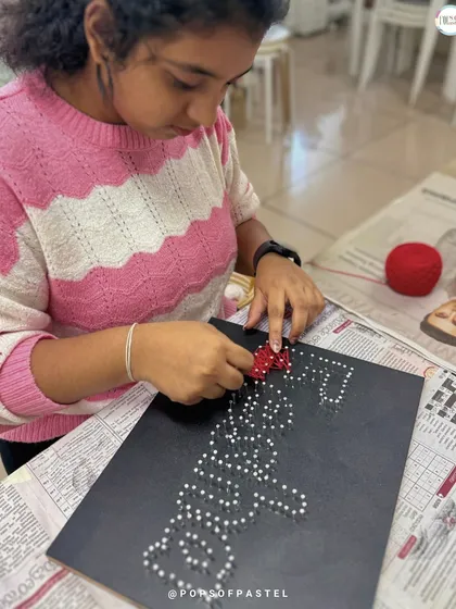 Adding the final touches to a custom name board, this participant weaves red string to create a heart.
