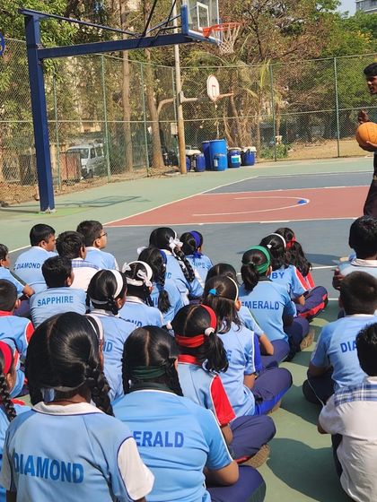A coach instructs a large group of students on a basketball court. This demonstrates our ability to manage and effectively teach large groups, ensuring every child is engaged.