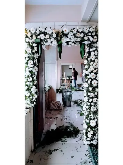A clean and elegant entrance for a marriage hall, crafted with an arch of white chrysanthemums and fresh green leaves. The image also shows our team during the setup process, ensuring every detail is perfect.