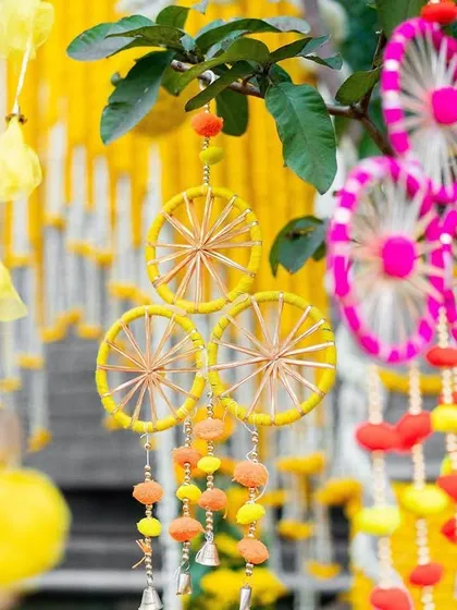 A close-up of the quirky and colorful decorative hangings used in a Mehendi setup. These handcrafted dreamcatchers and tassels add a playful and personalized touch to the decor.