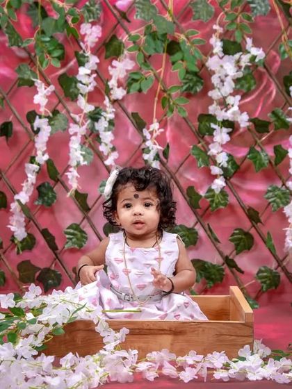 A lovely studio portrait with a pink floral theme. This little girl is sitting in a wooden box, surrounded by a wall of hanging flowers.