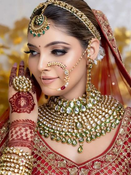 A stunning close-up of a bride with intricate henna and beautiful green and white jewelry. The makeup features a classic winged liner and flawless skin.