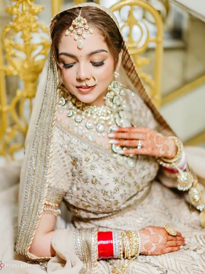 A serene portrait of the Sikh bride in her ivory and gold wedding attire, looking down at her intricate henna design.