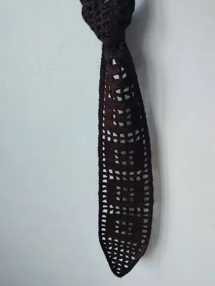 A hanging shot of the filet crochet tie, highlighting its geometric pattern.