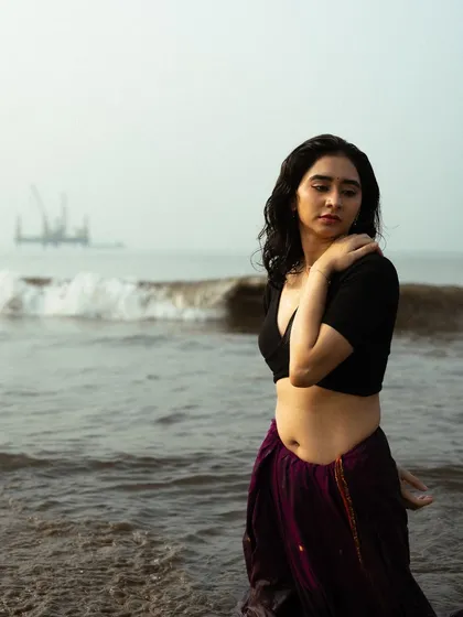 A pensive moment in the waves. The misty, atmospheric background with the distant structure adds a layer of mystery to the portrait.