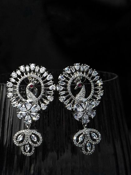 Peacock-inspired earrings shot with dramatic lighting against a dark glass. This creative approach makes the product look dynamic and luxurious.