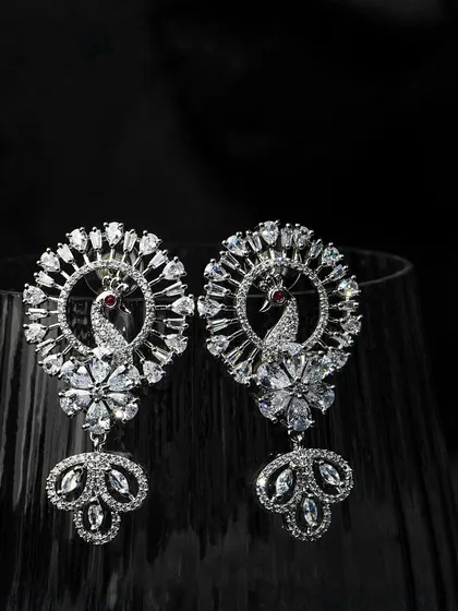 Peacock-inspired earrings shot with dramatic lighting against a dark glass. This creative approach makes the product look dynamic and luxurious.