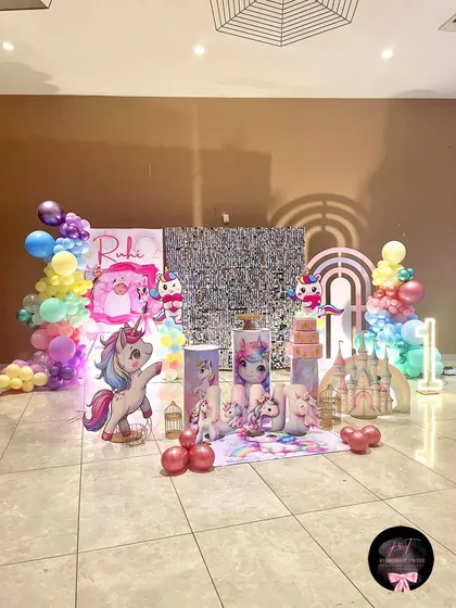 A dreamy unicorn-themed first birthday party for Ruhi. The setup includes a shimmering silver backdrop, pastel balloon garlands, custom unicorn cutouts, and personalized props to create a magical atmosphere.