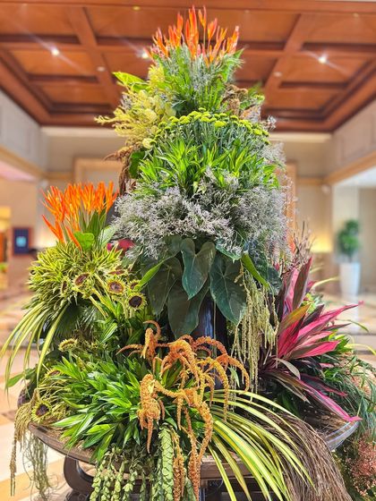 A vibrant and lush green arrangement with pops of orange and deep red, showcasing a more tropical and colorful take on foliage-based design.