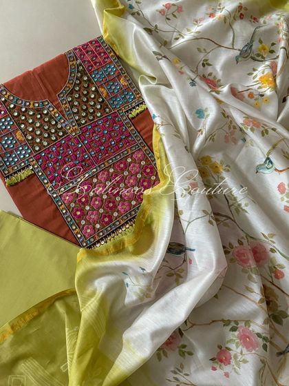 A rust-colored handloom cotton kurta with a heavily embroidered yoke, paired with a hand-painted dupatta featuring birds and blossoms on a white and lime green base.
