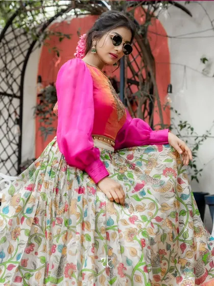 A fusion of art and fashion. This unique lehenga features a hand-painted Kalamkari silk skirt, showcasing traditional motifs. It is paired with a contemporary pink blouse with dramatic puff sleeves, creating a bold and artistic statement.