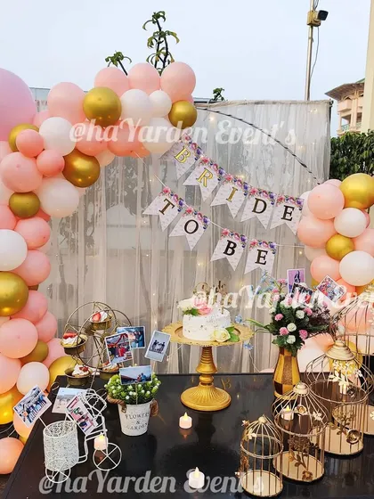 An outdoor 'Bride to Be' party on a terrace. The setup includes a balloon arch, a cake table, and decorative props.