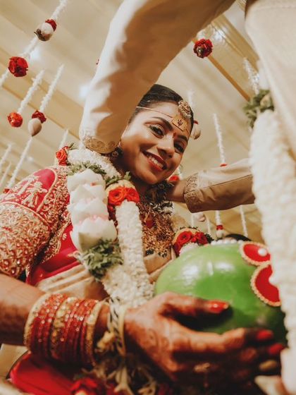 A candid moment during a wedding ritual, with the bride smiling as she holds a coconut.