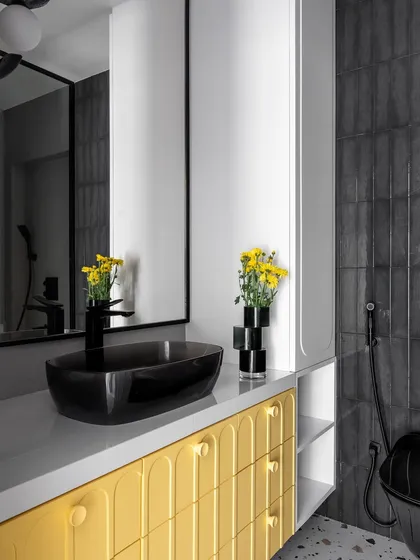 This bathroom makes a statement with a bright yellow vanity featuring custom arched detailing. Paired with a black vessel sink and modern floral pendant lights, the space is playful, bold, and full of personality.