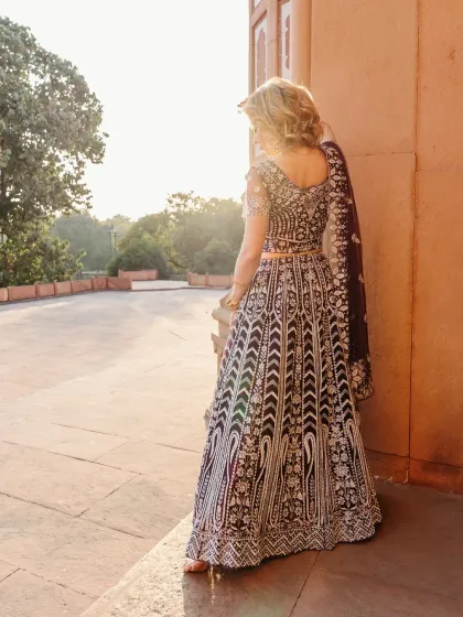 A back view of the model in her ornate lehenga, set against the backdrop of golden hour light. This perspective emphasizes the detailed craftsmanship of the traditional Indian garment.